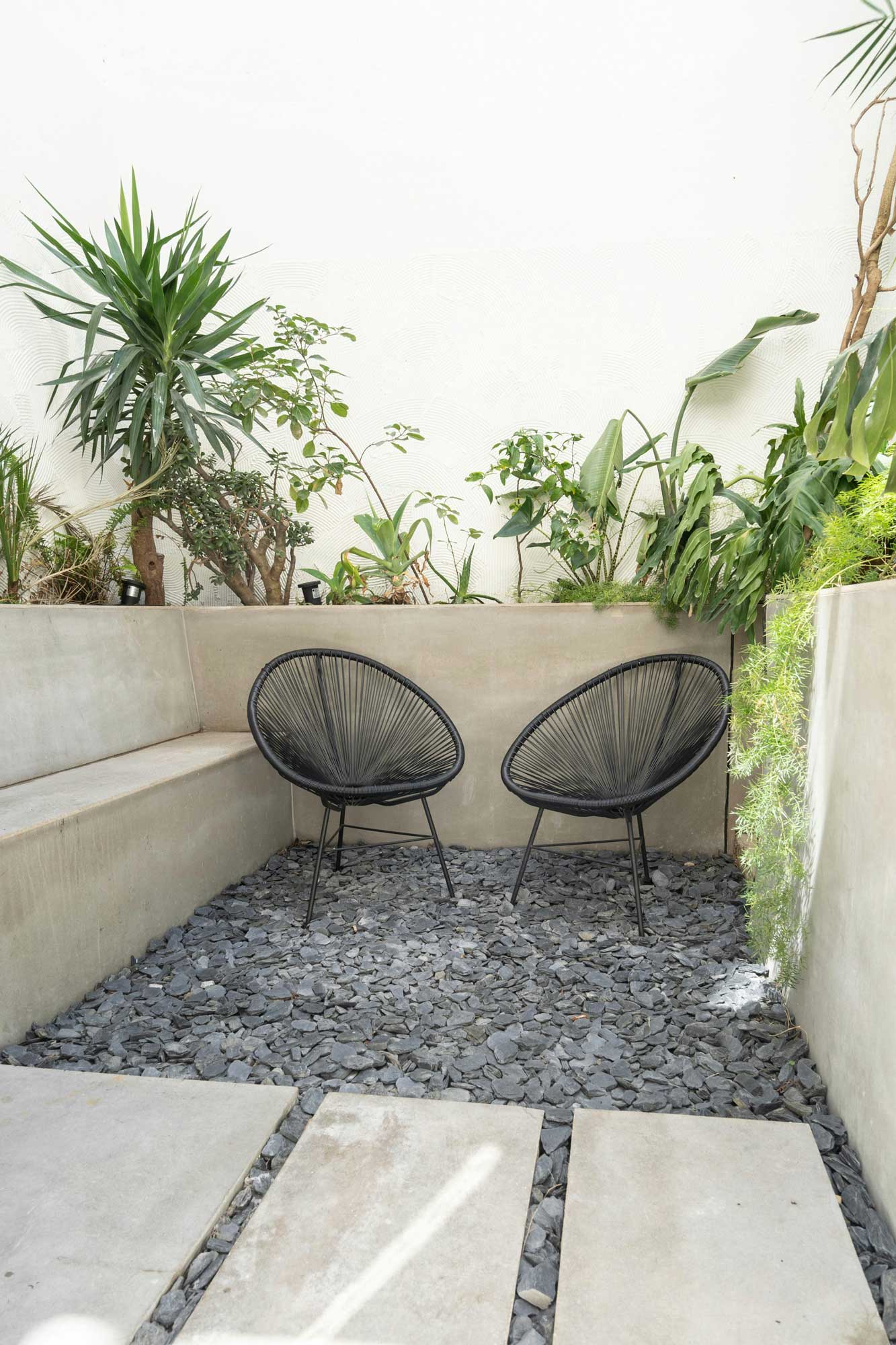 Kleine Sitzecke aus Beton gebaut, mit Betonwänden und Betonstufen. Im Hintergrund Pflanzen, im Zentrum 2 Stühle.