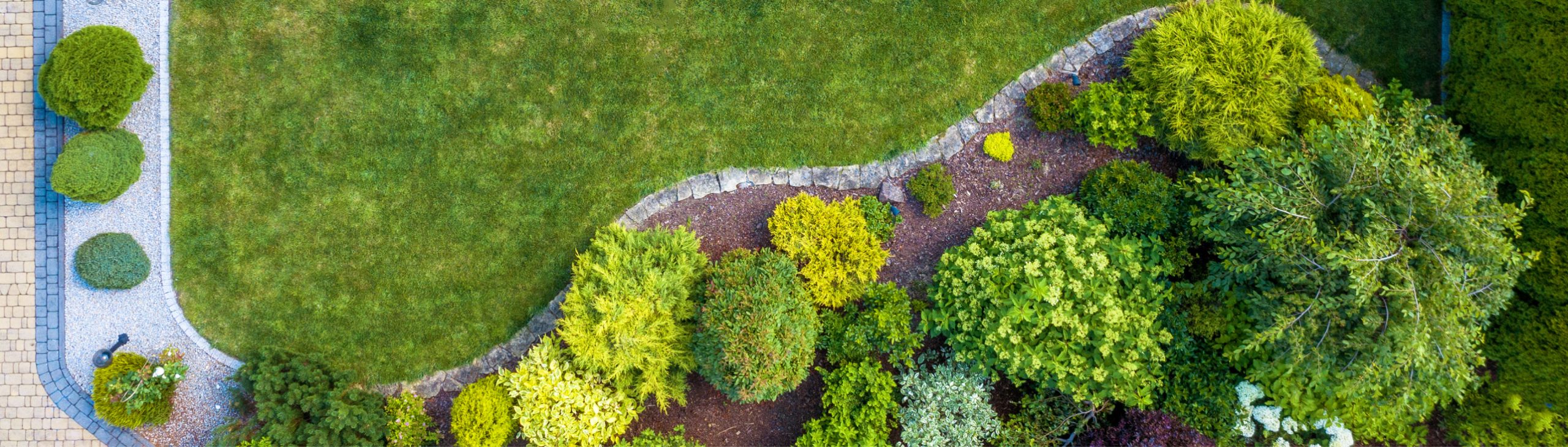 Topshot eines Gartens mit Grünfläche und Bepflanzung.